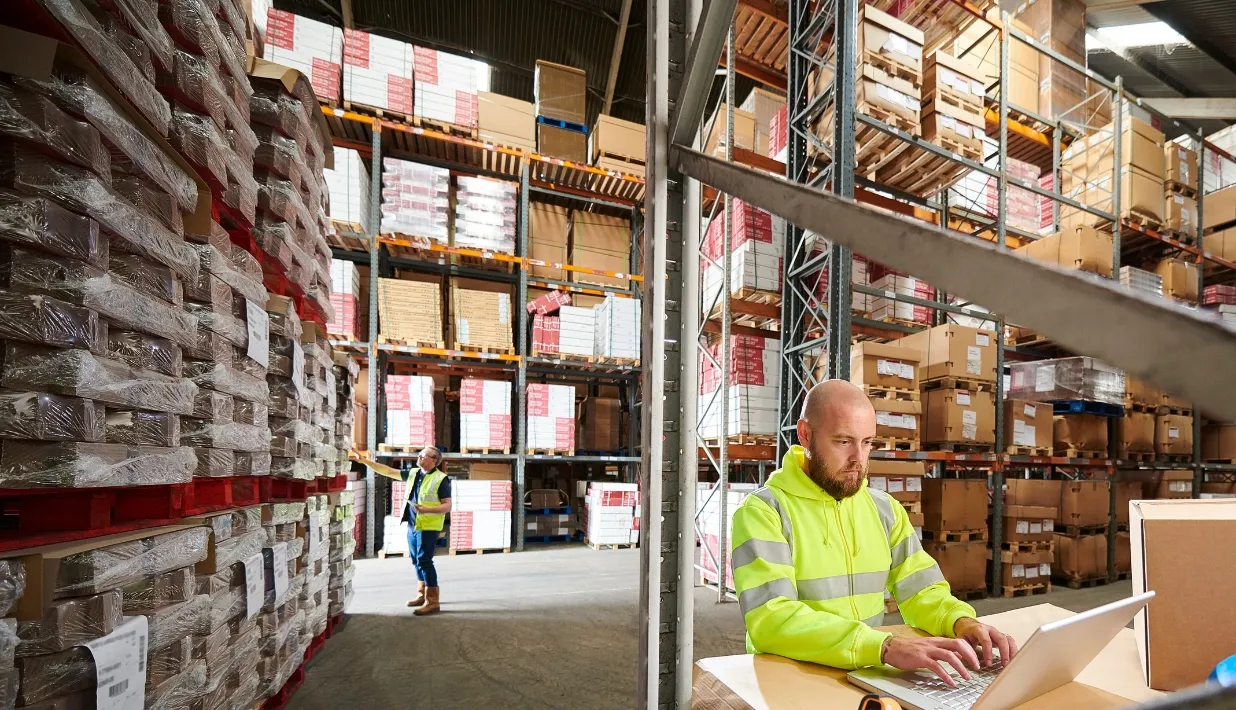 Warehouse operator reviewing a carton workflow among racked inventory